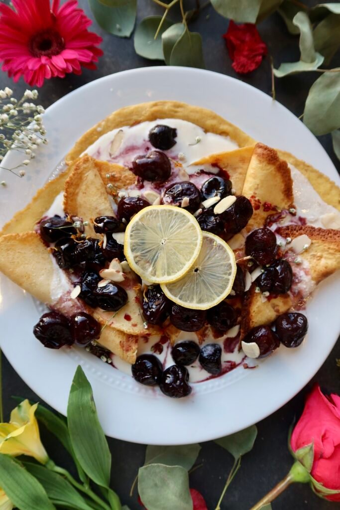 High protein almond cherry crepes stacked and topped with fresh cherries and almond cream