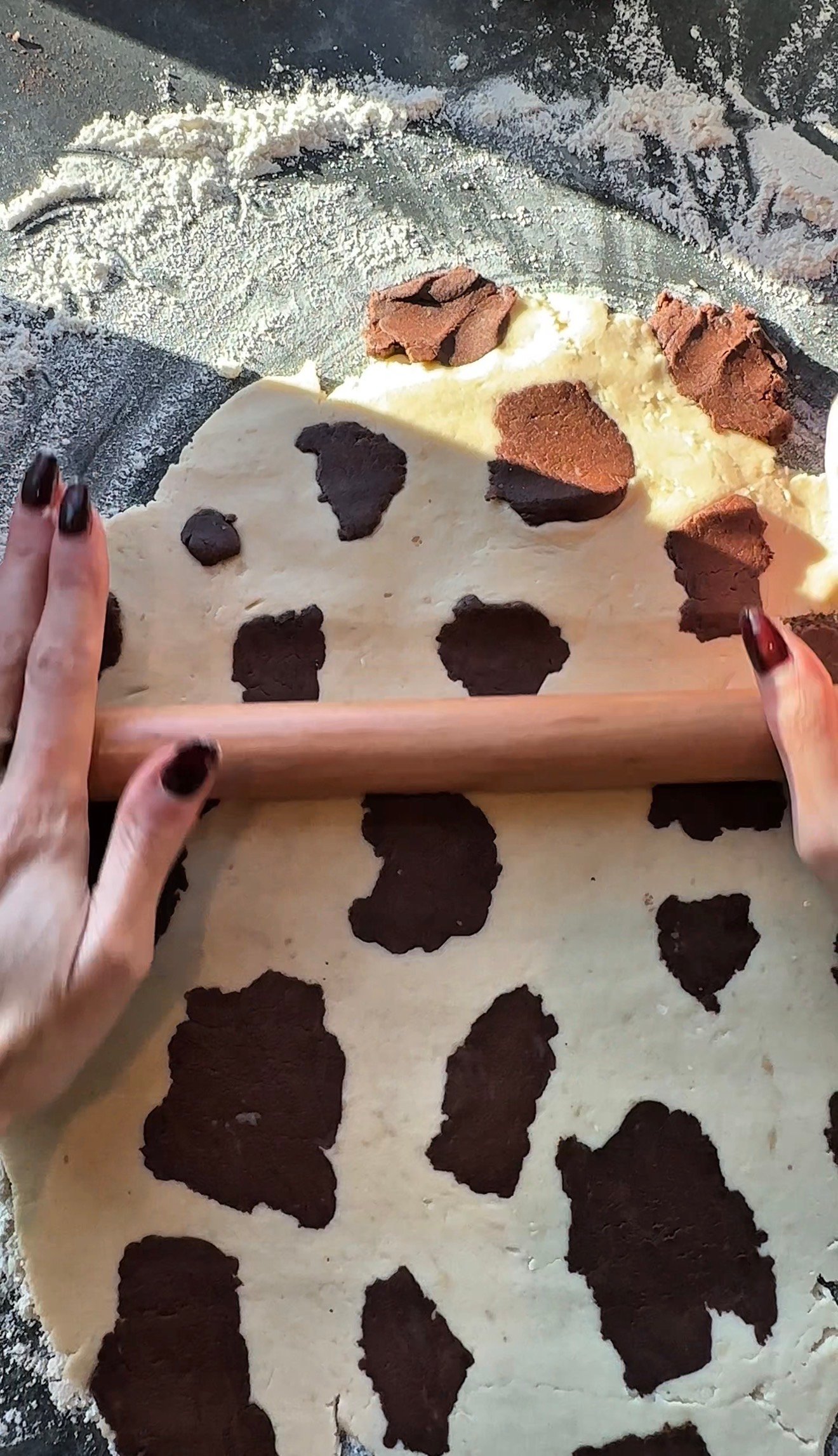 Chocolate brown dough pieces pressed into vanilla dough to create cow spot pattern for Christmas cookies