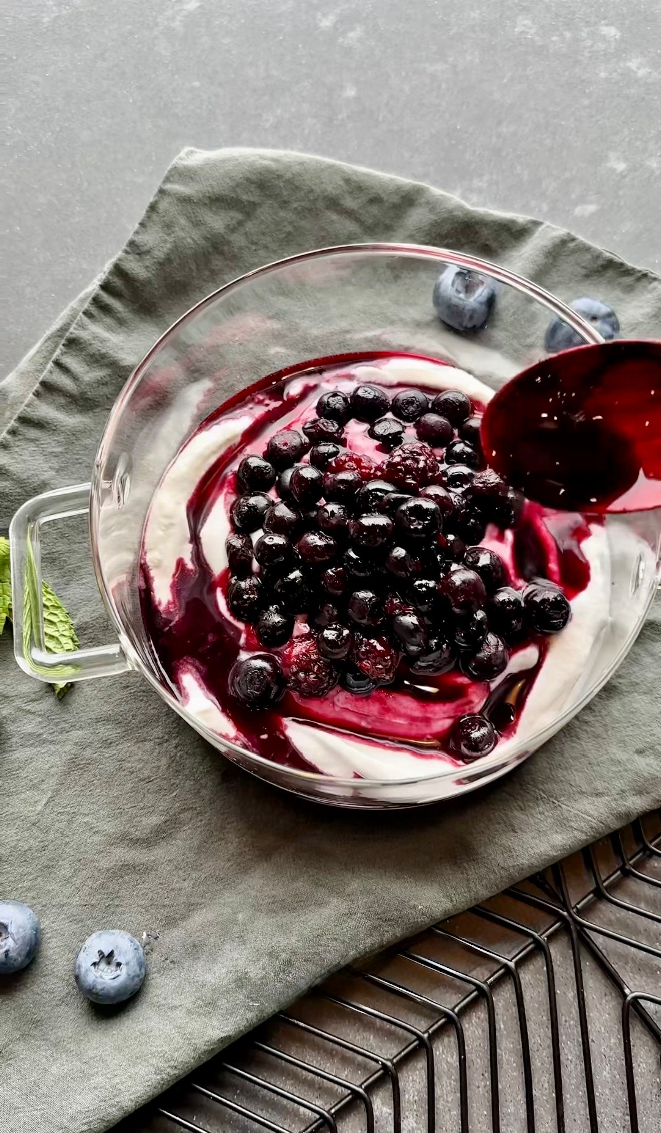 Warm blueberry compote being spooned over plain coconut yogurt in a bowl