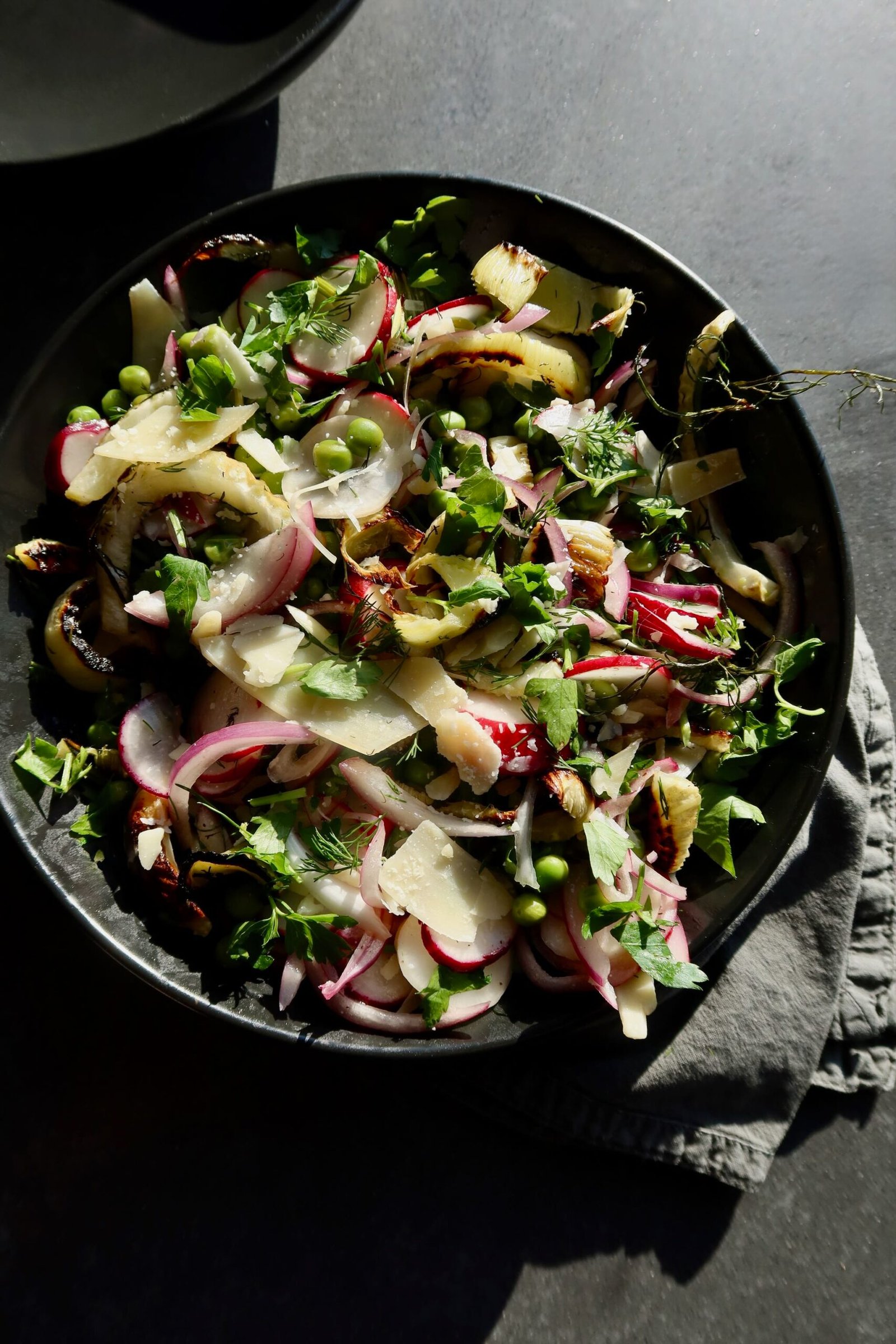 Bright spring salad with roasted fennel sweet peas radish pistachios and shaved Parmesan on a platter