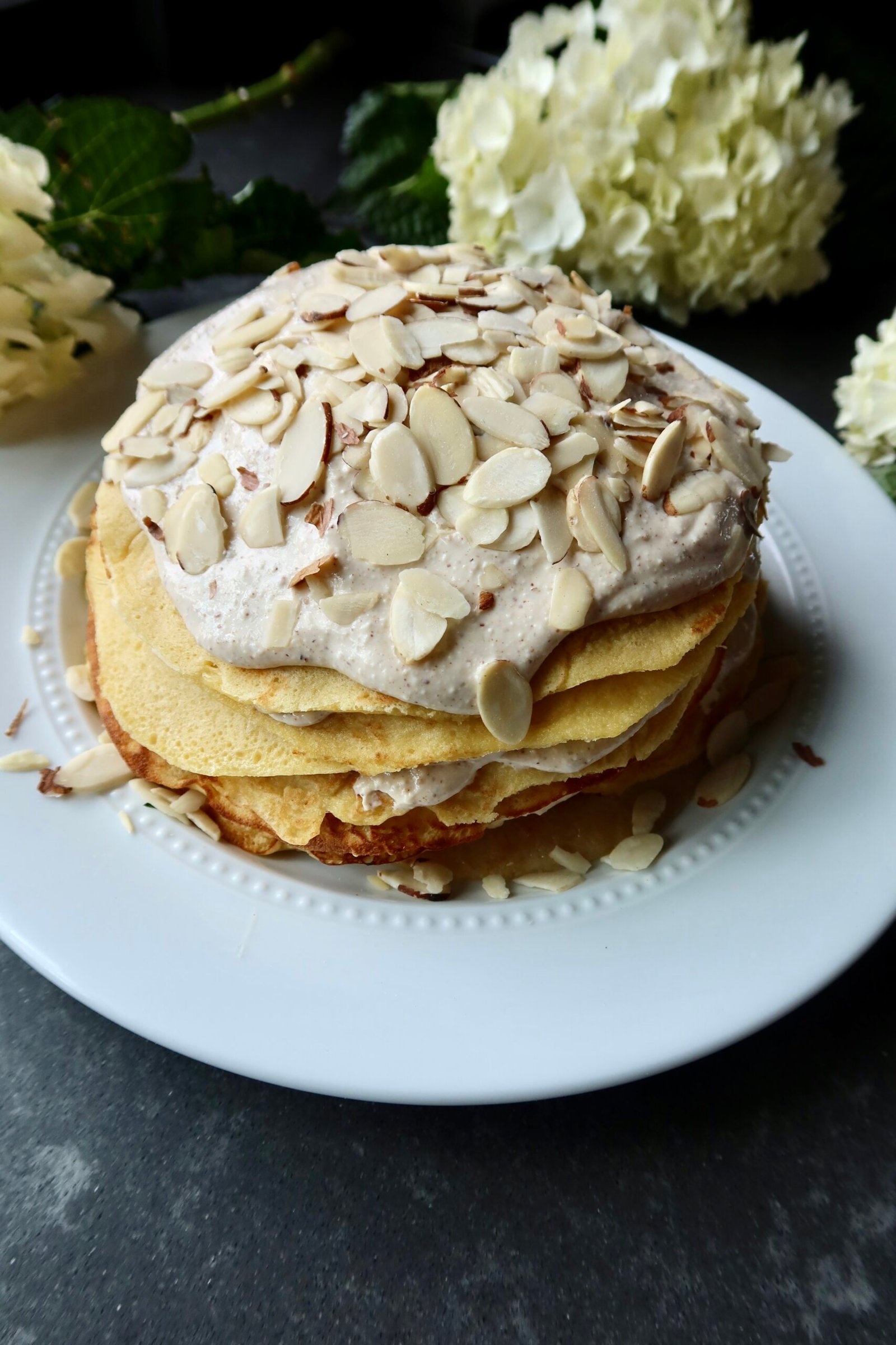 High protein almond croissant crepe stack layered with almond cream and topped with sliced almonds and powdered sugar